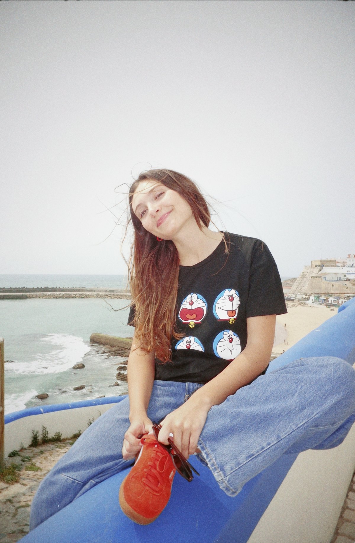 Carolina sentada num muro azul junto ao mar
